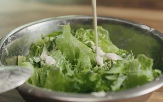 closeup mixing frillis salad leaves with caesar sauce