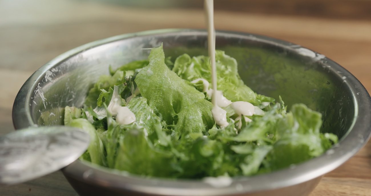 closeup mixing frillis salad leaves with caesar sauce